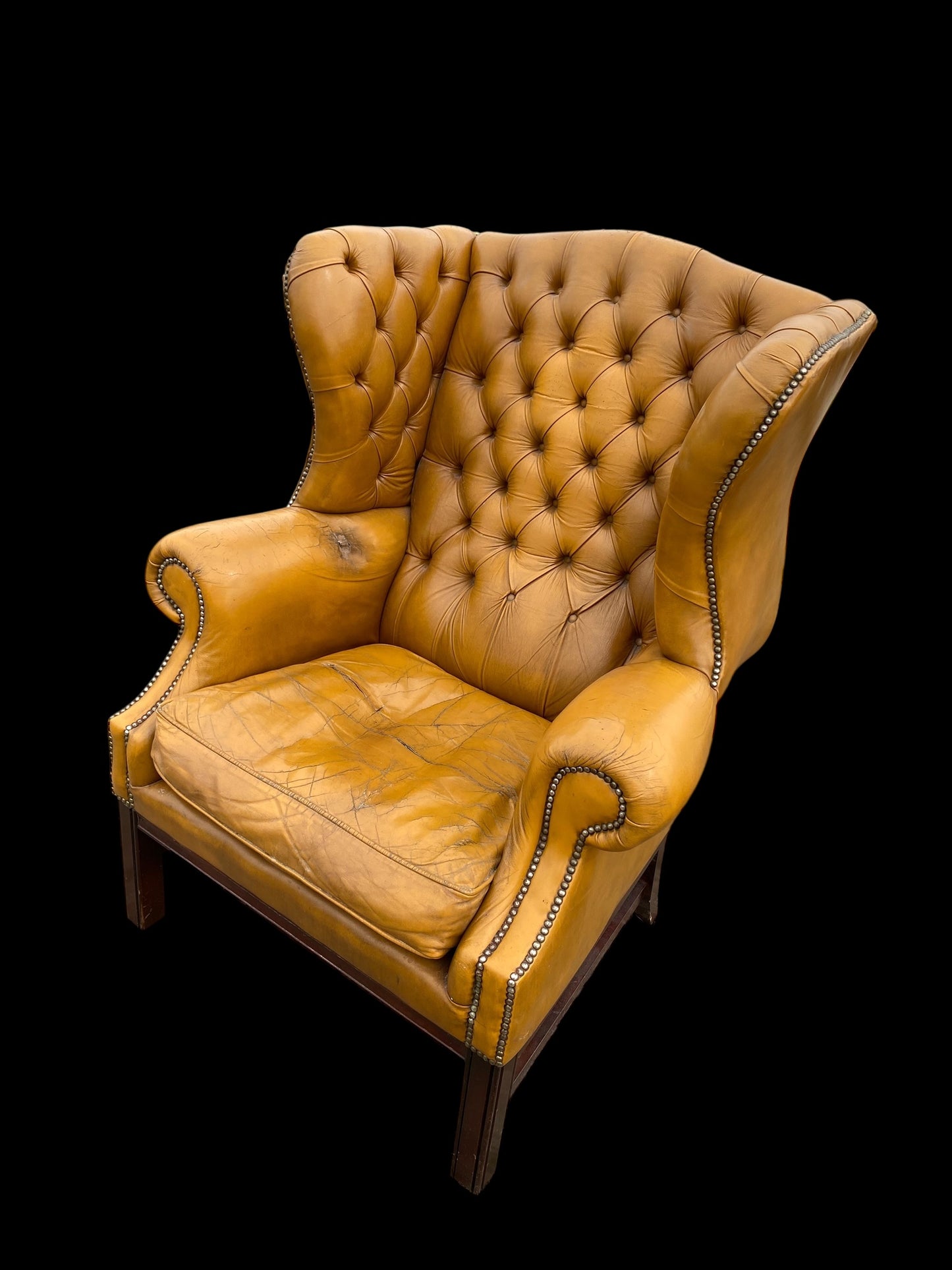 A VERY large, well worn, mustard coloured leather Chesterfield style wingback chair