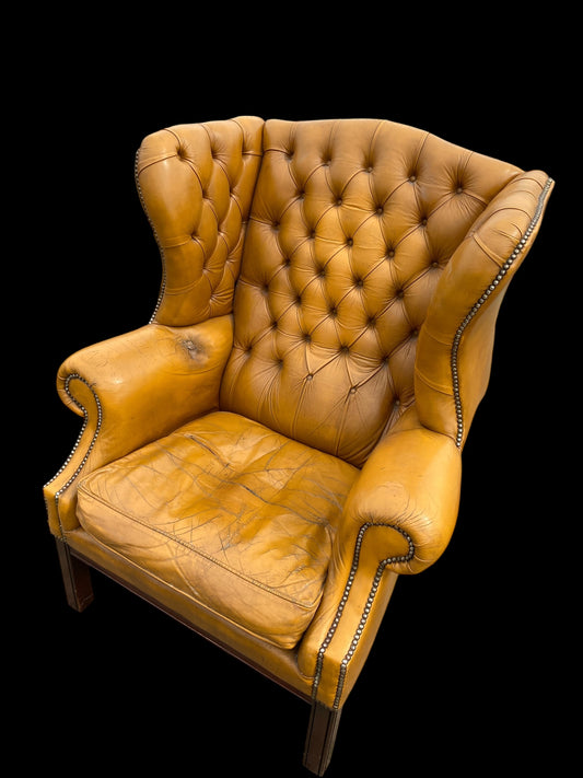 A VERY large, well worn, mustard coloured leather Chesterfield style wingback chair